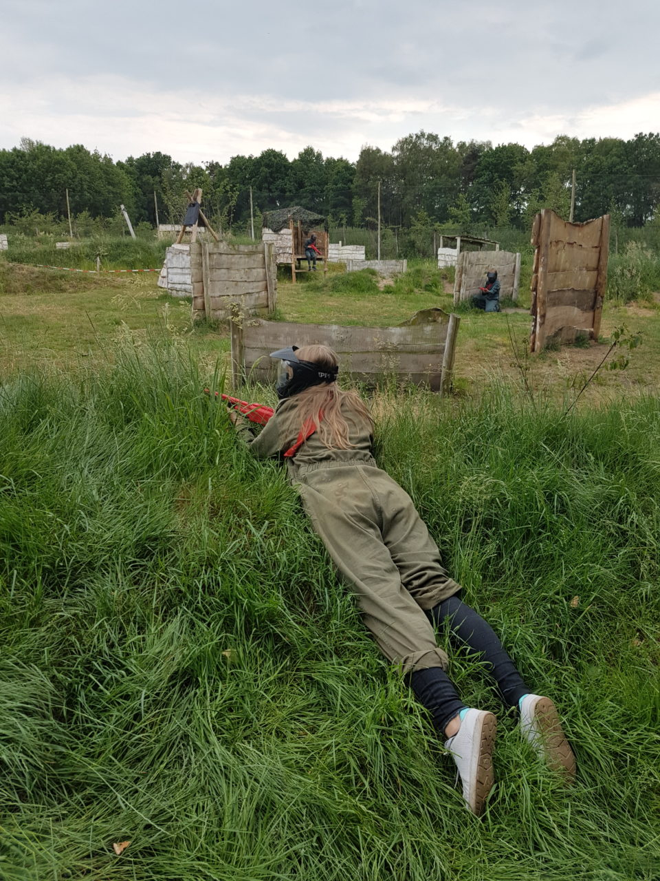 Mädchen liegt auf einem Hügel im Kinderpaintballfeld