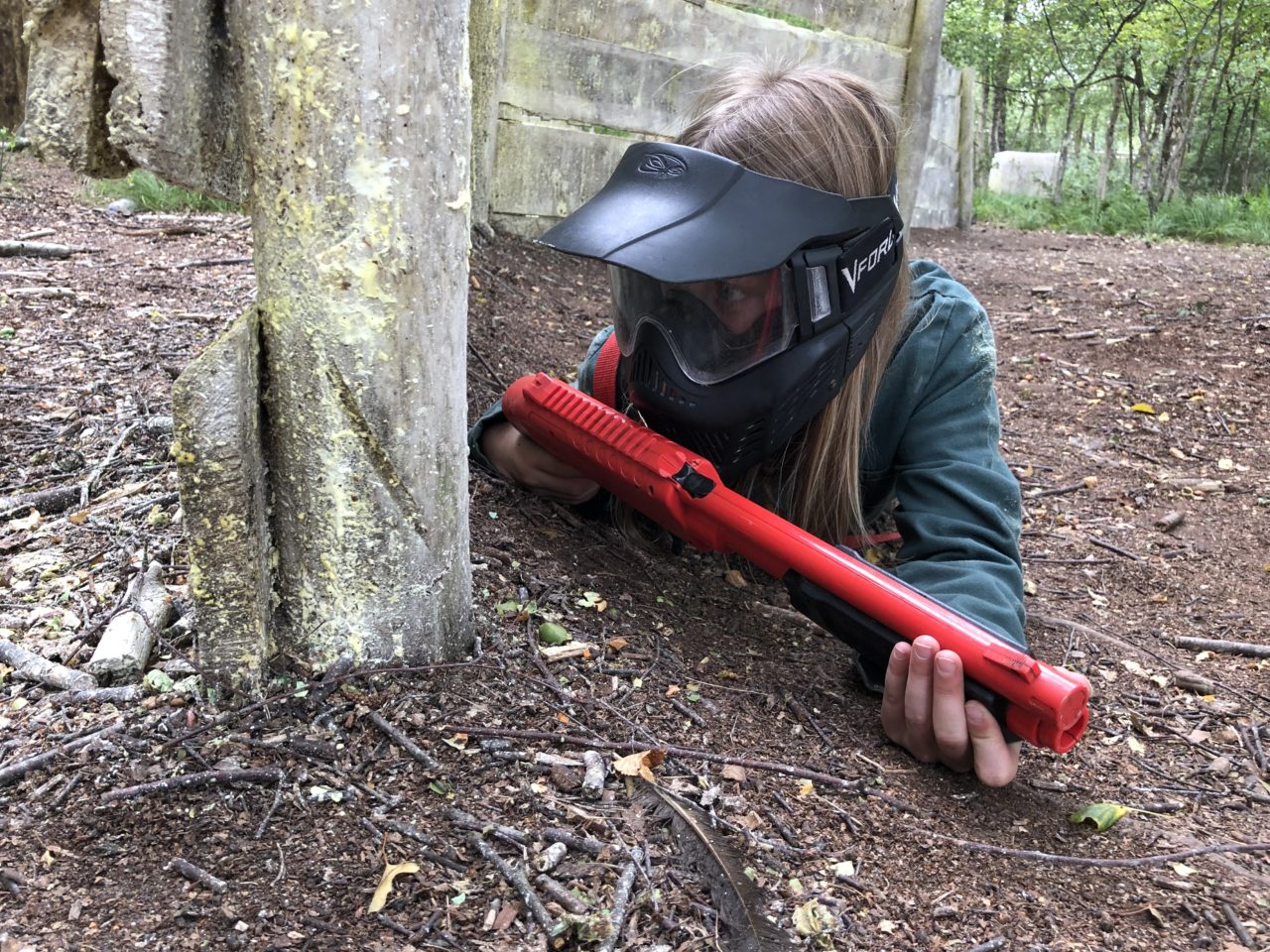 Mädchen schleicht sich durch Paintballwald und behält den Gegner im Auge.