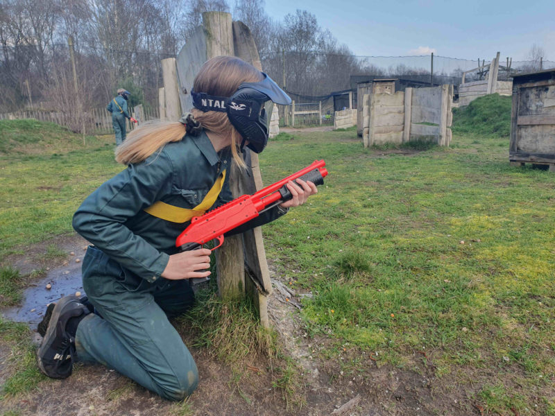 Meisje kijkt vanachter dekking op een paintball kinderfeestje